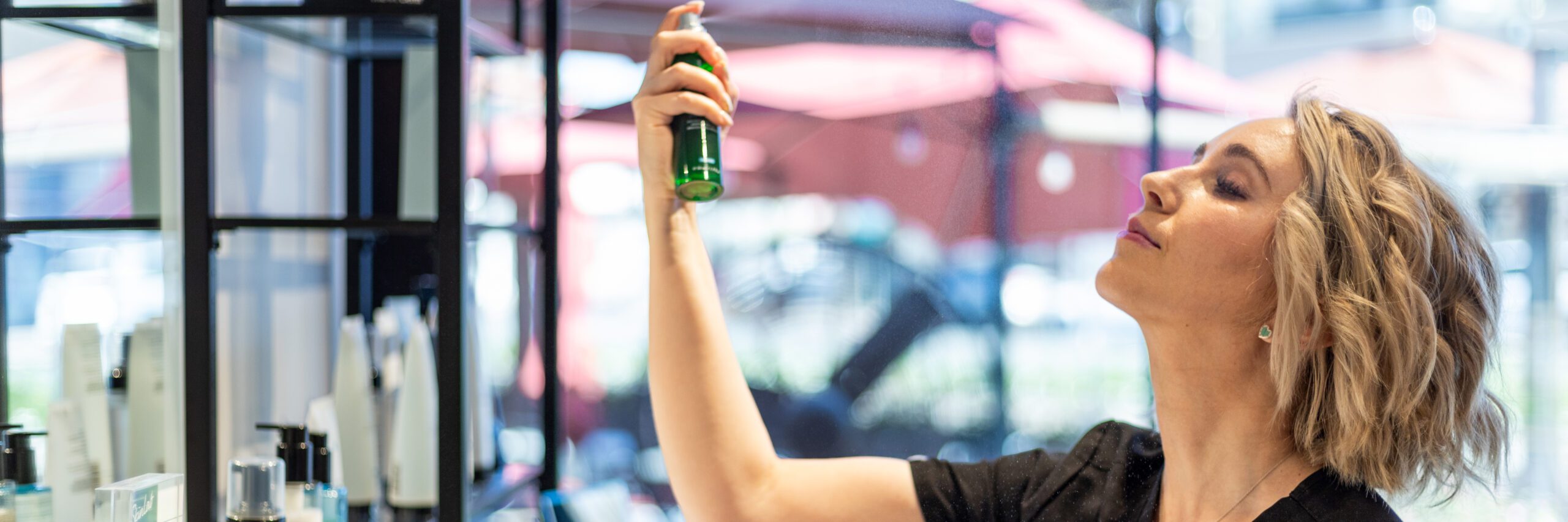 Esthetician in front of a product counter spraying a product from a green bottle on her face