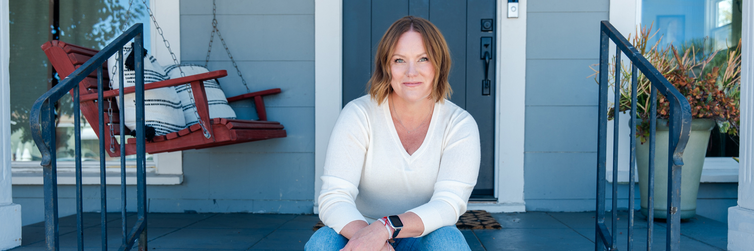 Courtney Murphy sitting on the front steps of her home. She's wearing a white shirt and jeans.