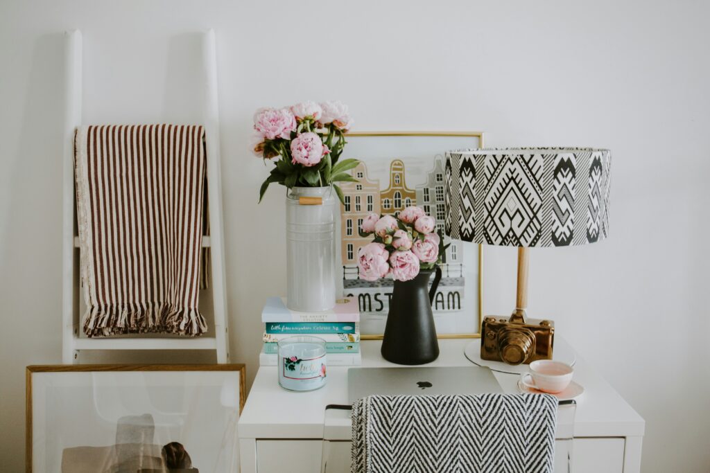 At home office desk. Decorated with pink flowers, a framed picture, candle, books and a lamp and few other items.