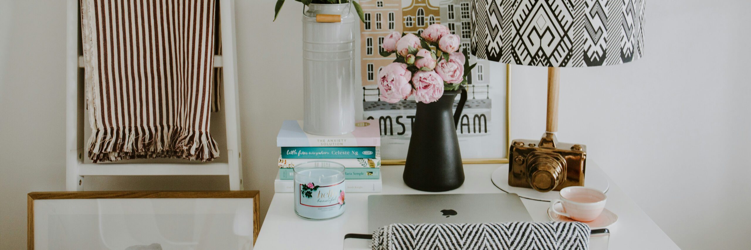 At home office desk. Decorated with pink flowers, a framed picture, candle, books and a lamp and few other items.