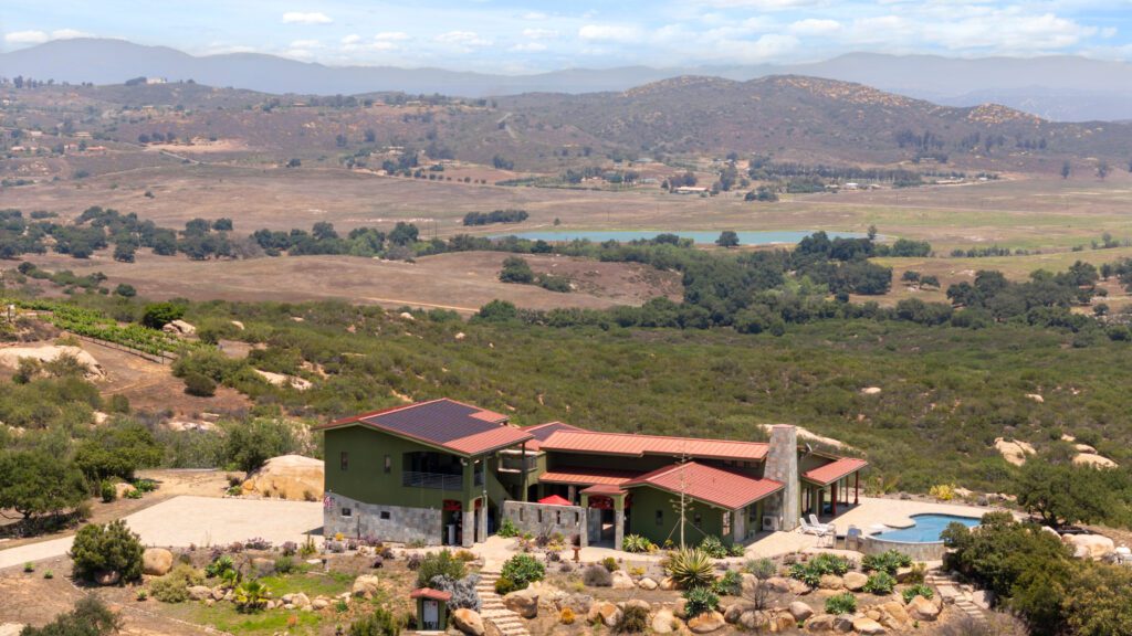 Aerial view of a green home with stone cladding and a pool looking out over the landscape of Ramona, California.
