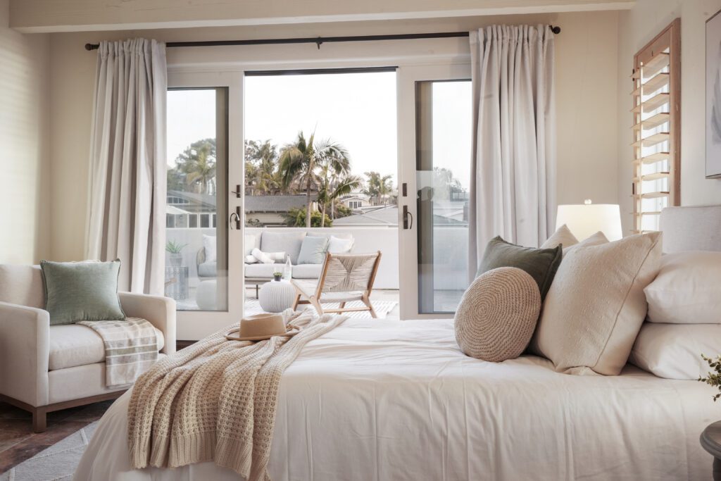 Staged cozy primary bedroom with a view of the bed, chair, and outdoor patio furniture on the balcony in Del Mar, California.